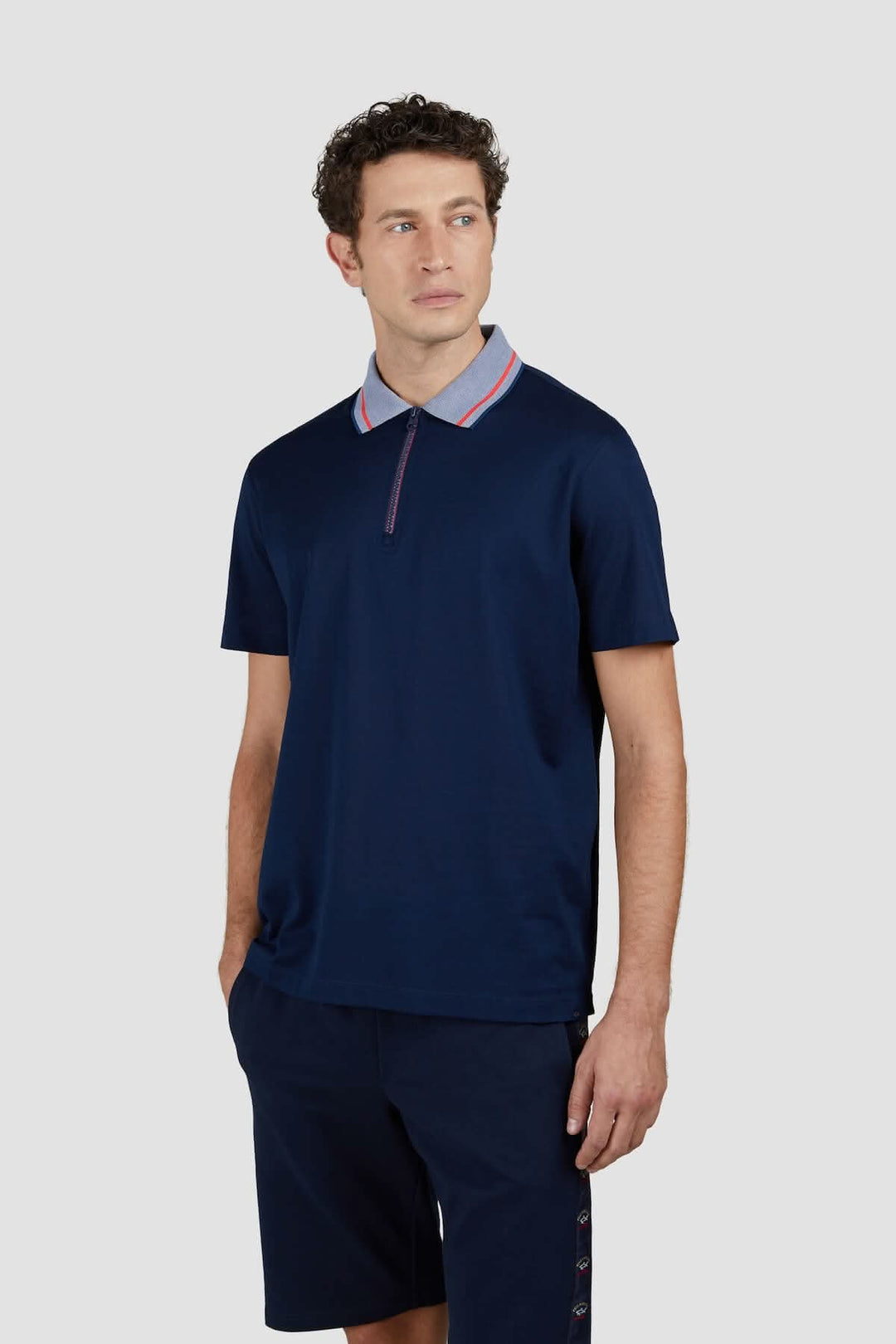 Homme portant un polo en coton bleu avec col contrasté gris et fermeture éclair, style décontracté.