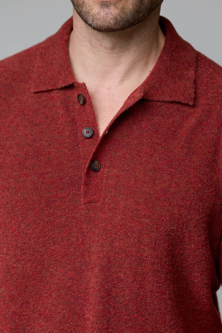 Homme portant un polo en laine mérinos rouge avec col classique et boutons.