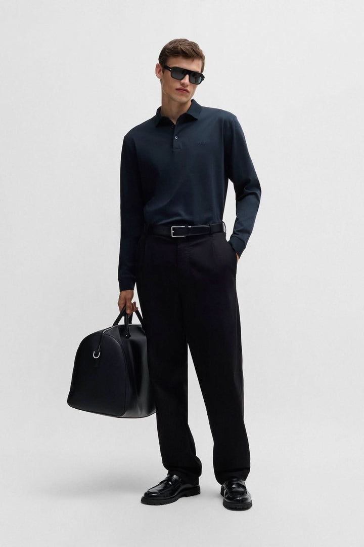 Homme portant un polo manches longues en coton noir, lunettes de soleil et sac, style élégant.