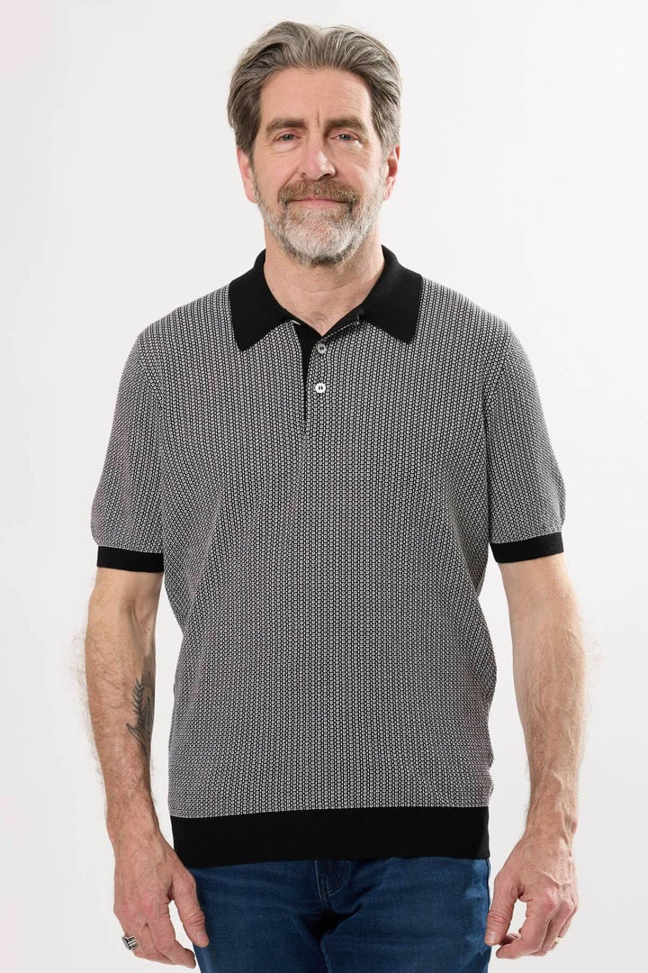 Homme portant un polo à micro-motif noir et blanc avec col contrastant, parfait pour une tenue estivale.