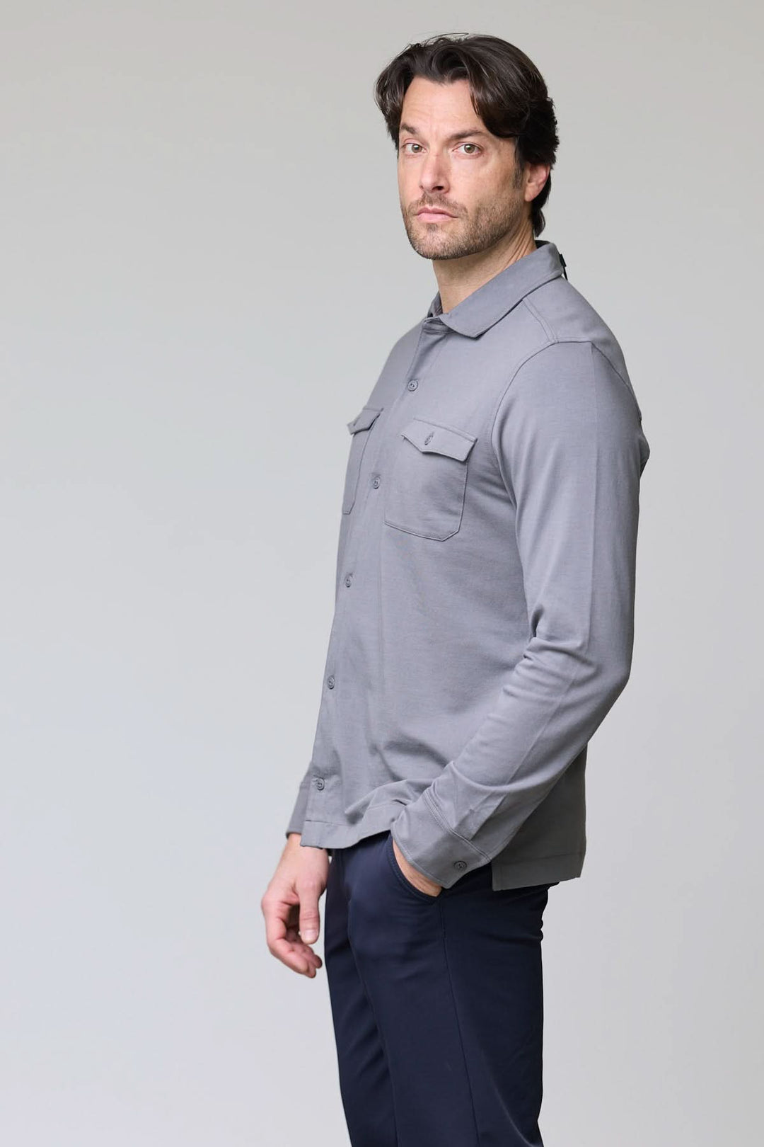 Homme portant un polo à poches boutonnées gris, manches longues, col chemise, look chic et décontracté.