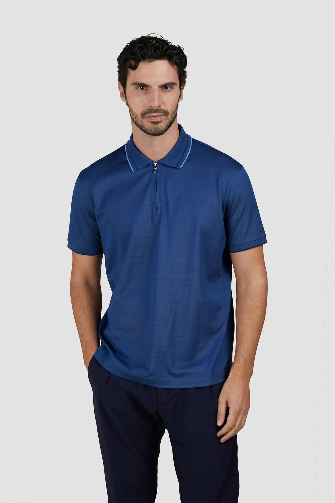 Homme portant un polo zippé en coton bleu, alliant élégance et confort avec détails contrastés au col.