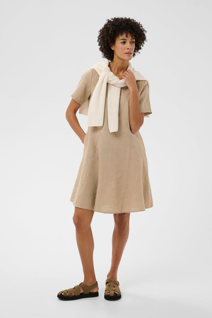 Femme portant une Robe Aminasa beige à manches courtes avec encolure en V, style décontracté et élégant. Idéale pour sorties estivales.