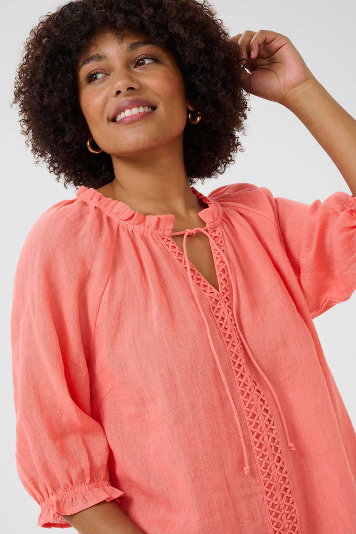 Femme souriante portant une robe en lin rose, avec encolure fendue et détails en dentelle, parfaite pour l'été.