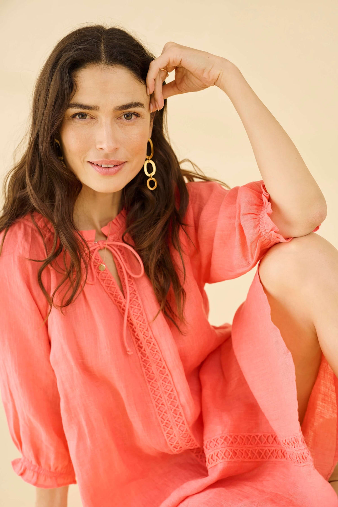 Femme souriante portant une robe en lin rose avec des détails en dentelle, parfaite pour les journées ensoleillées.