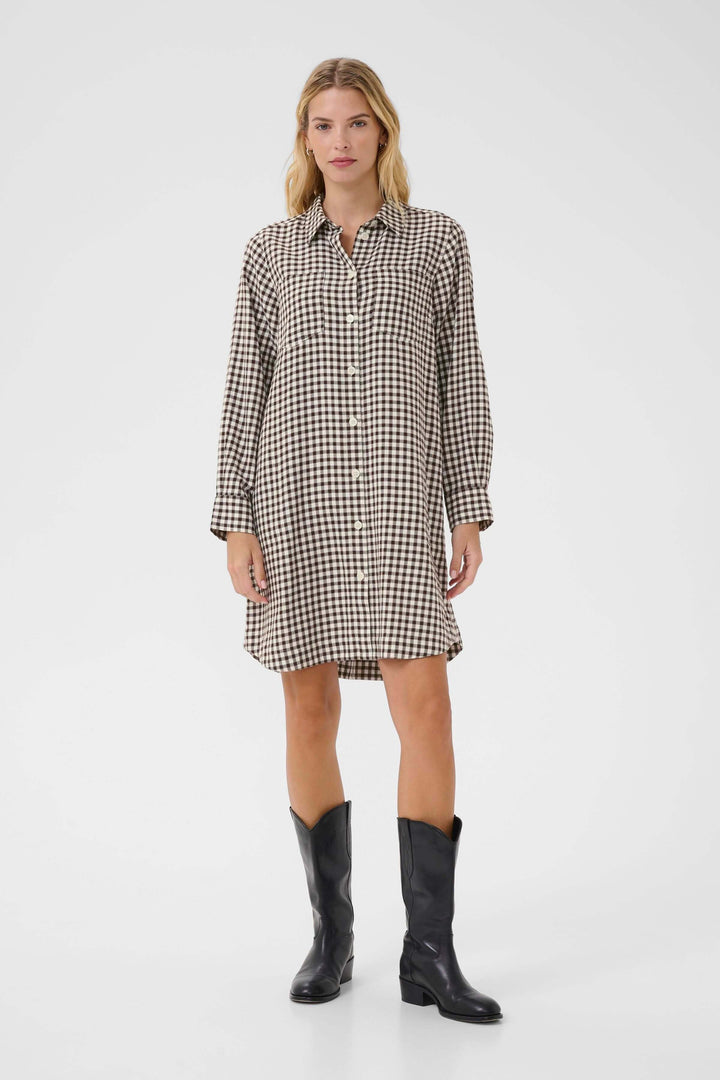 Femme portant la Robe Sardias à carreaux, coupe droite et manches retroussables, style casual-chic avec bottes noires.