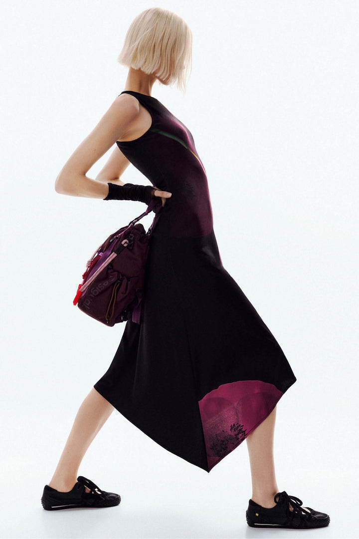 Robe asymétrique coquelicot avec imprimé floral artistique, portées par une femme avec sac à la main pour un look moderne et sophistiqué.