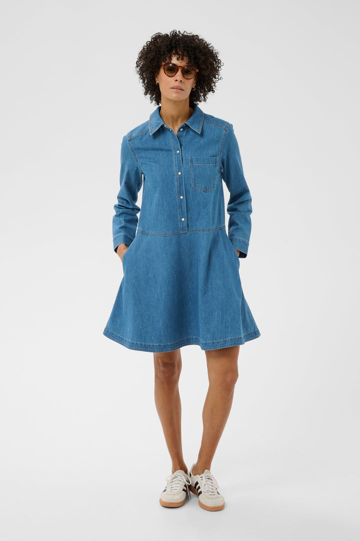 Robe chemise Augustine en denim avec coupe évasée, col chemise et manches longues, portée avec des espadrilles blanches et noires.