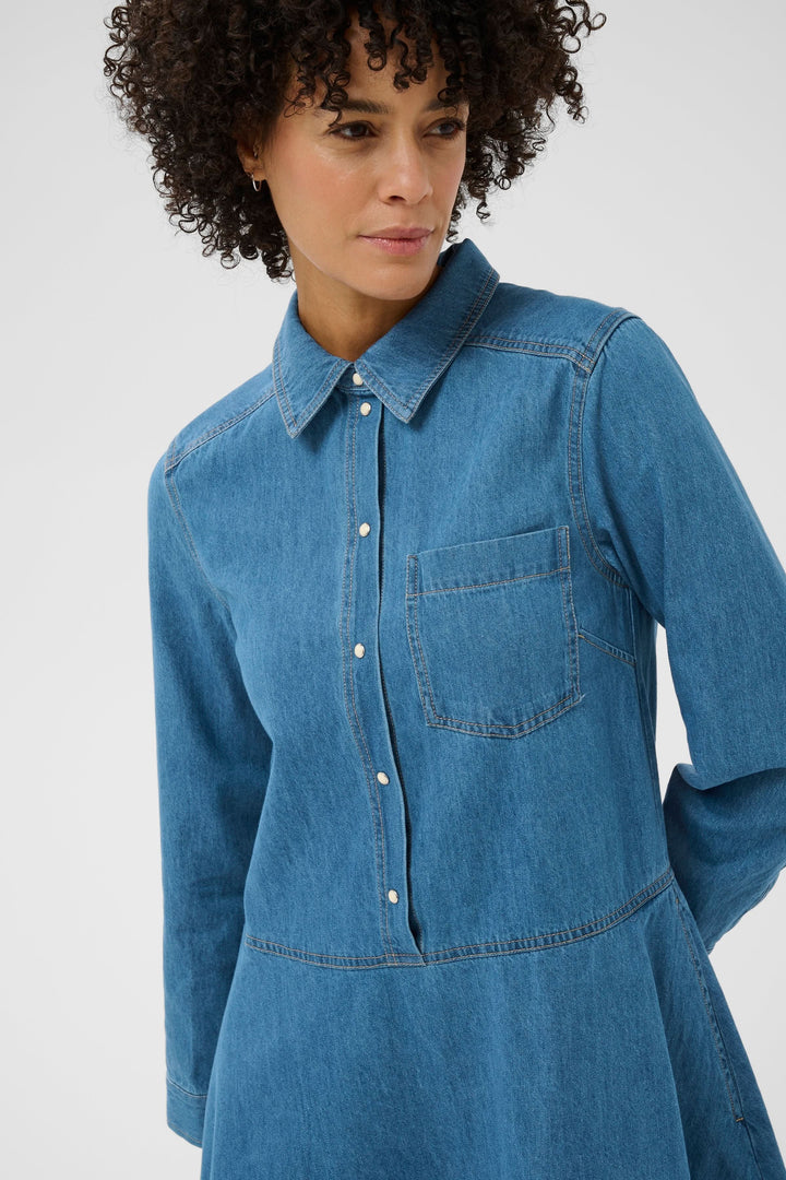 Femme portant la Robe chemise Augustine en denim, coupe évasée et col structuré, avec manches longues et poche poitrine.