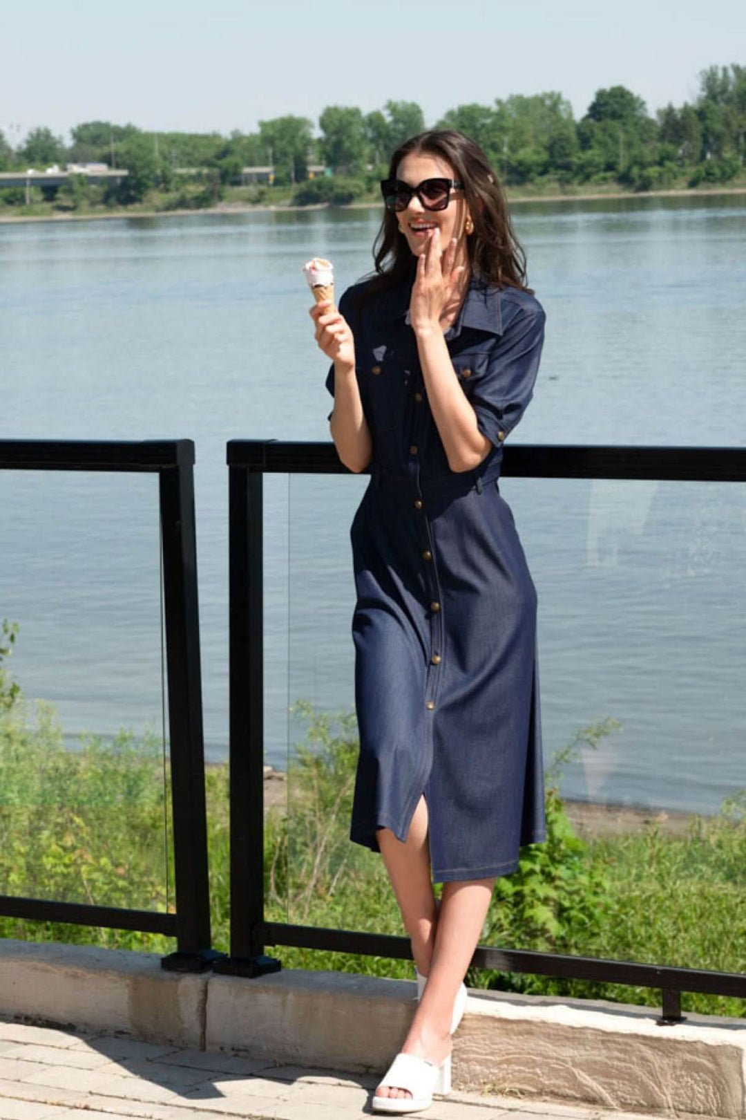 Femme en robe chemisier aspect denim dégustant une glace au bord de l'eau, style décontracté et élégant.