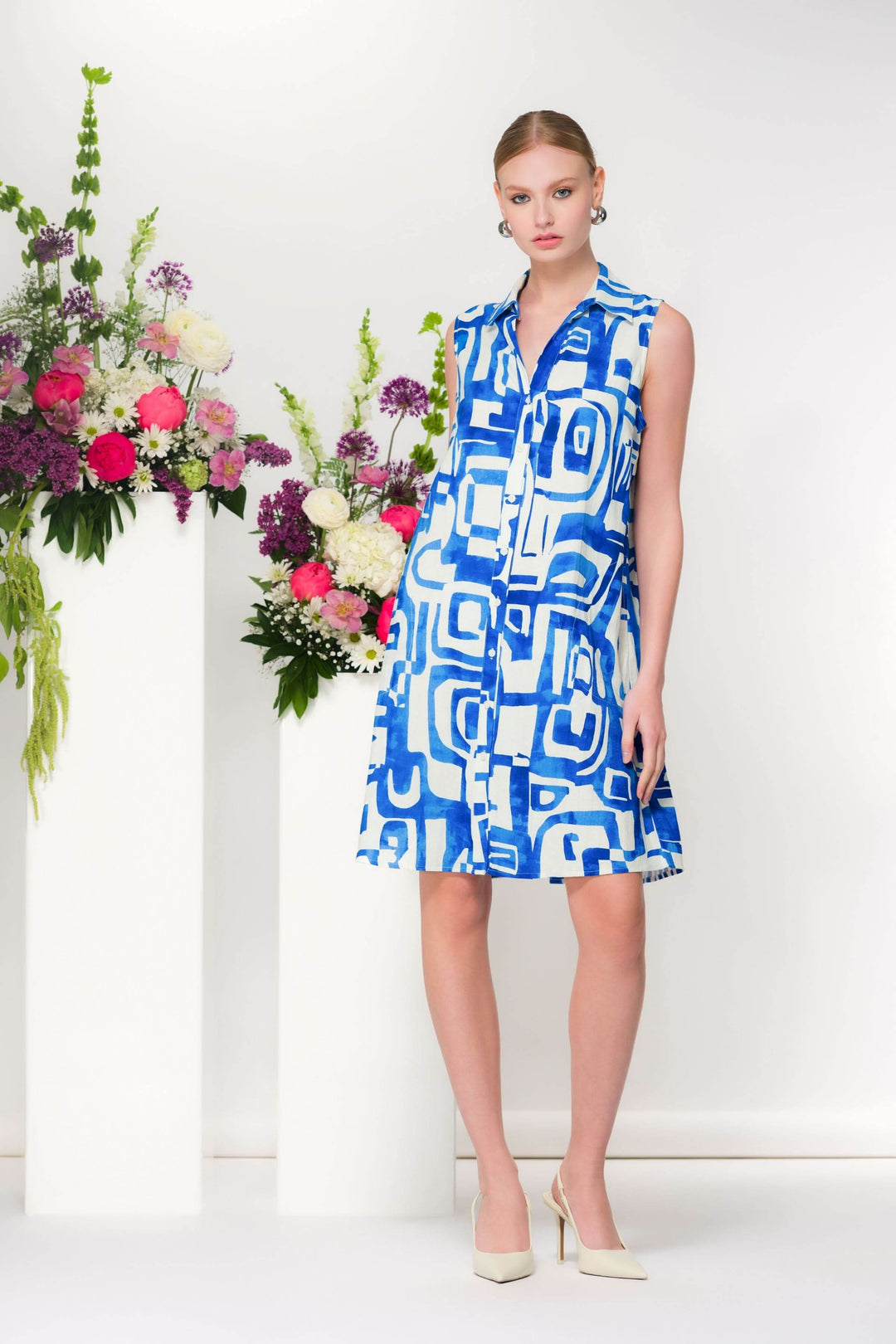 Robe col chemisier sans manches avec imprimé graphique bleu et blanc, coupe évasée, devant des fleurs décoratives.