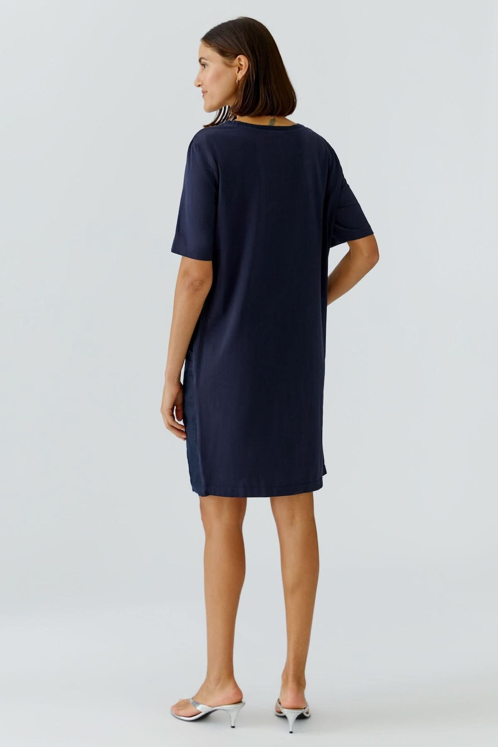 Femme portant une robe droite minimaliste manches courtes de couleur sombre, vue de dos, avec coupe épurée et longueur au genou.