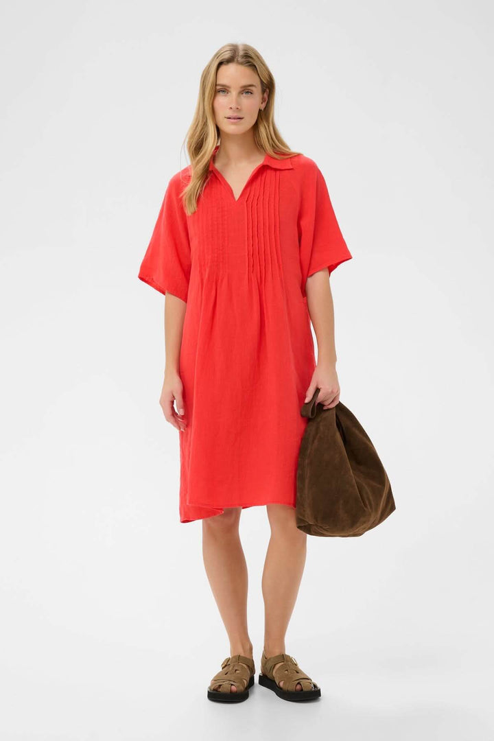 Robe en lin Ayla rouge avec coupe droite et détails plissés, portée par une femme avec un sac à main marron, idéale pour toutes occasions.
