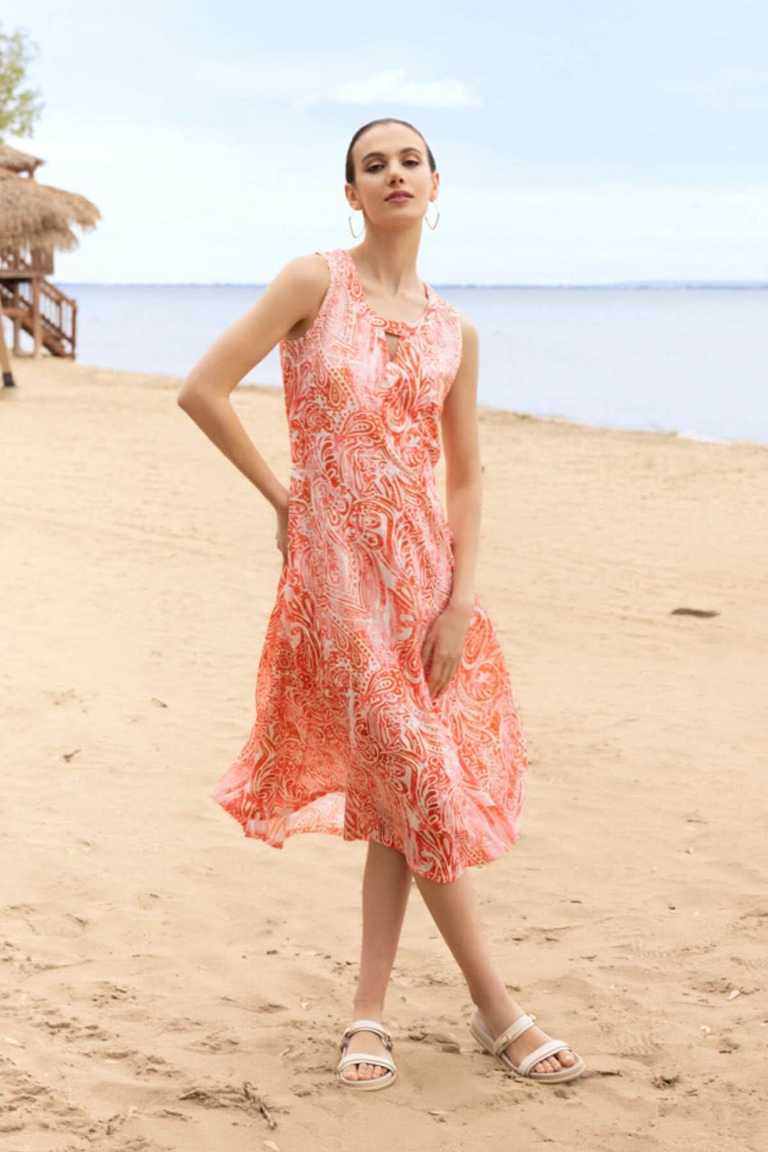 Femme portant une robe fluide imprimée sans manches sur une plage, idéale pour l'été et les escapades ensoleillées.