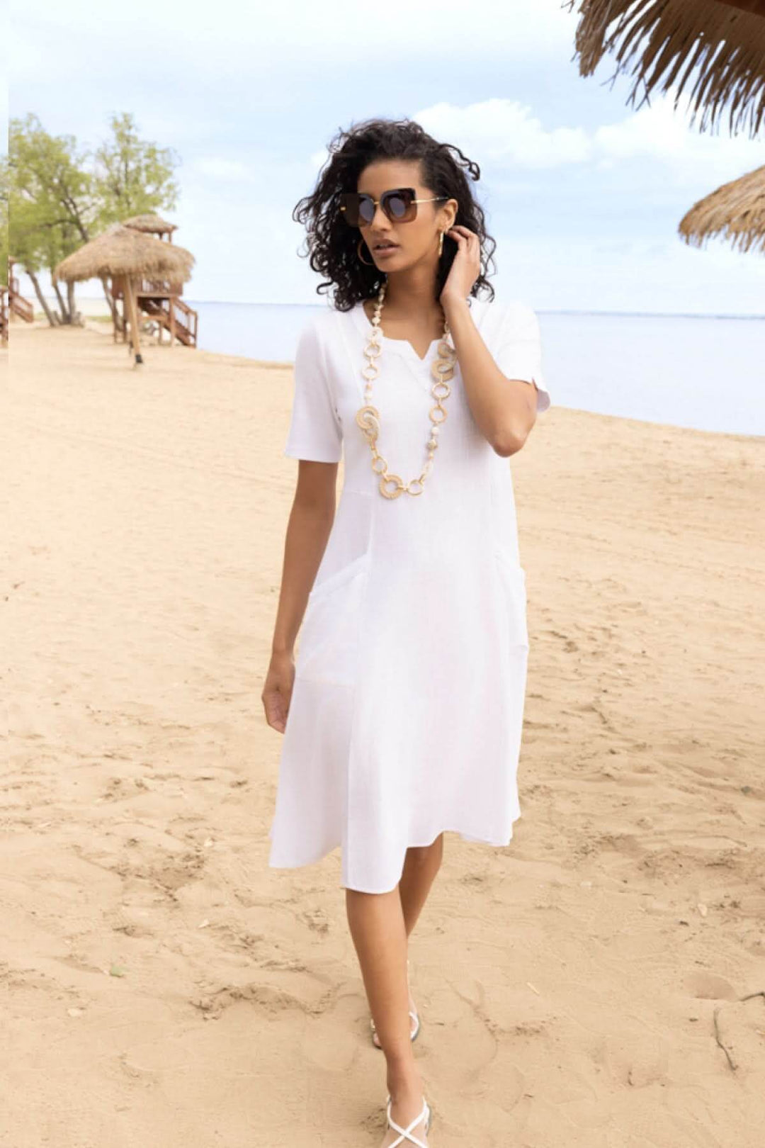 Femme portant une robe fluide manches courtes col fendu sur la plage, style estival décontracté.