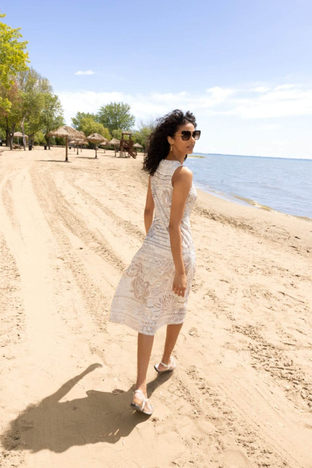 Robe imprimée sans manches portée sur une plage ensoleillée, offrant une coupe fluide et féminine pour un look estival élégant.