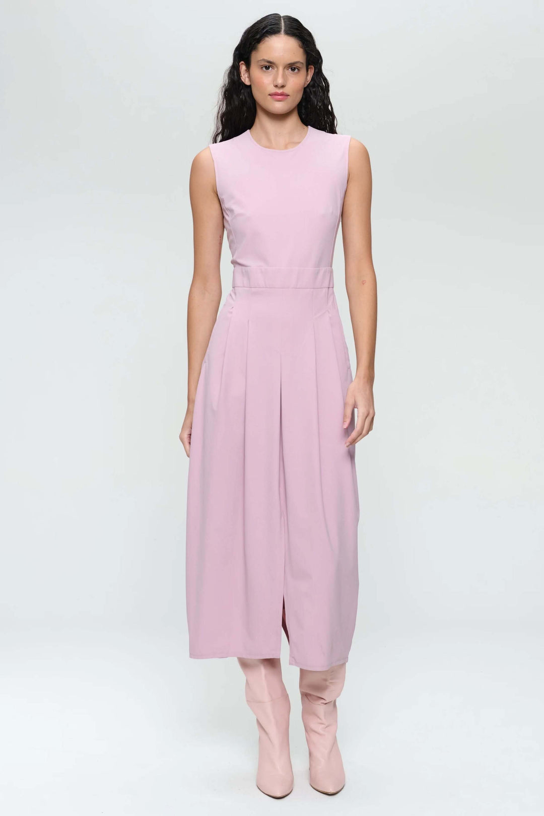 Robe longue sans manches rose avec encolure ronde et plis creux, portée avec des bottes hautes.