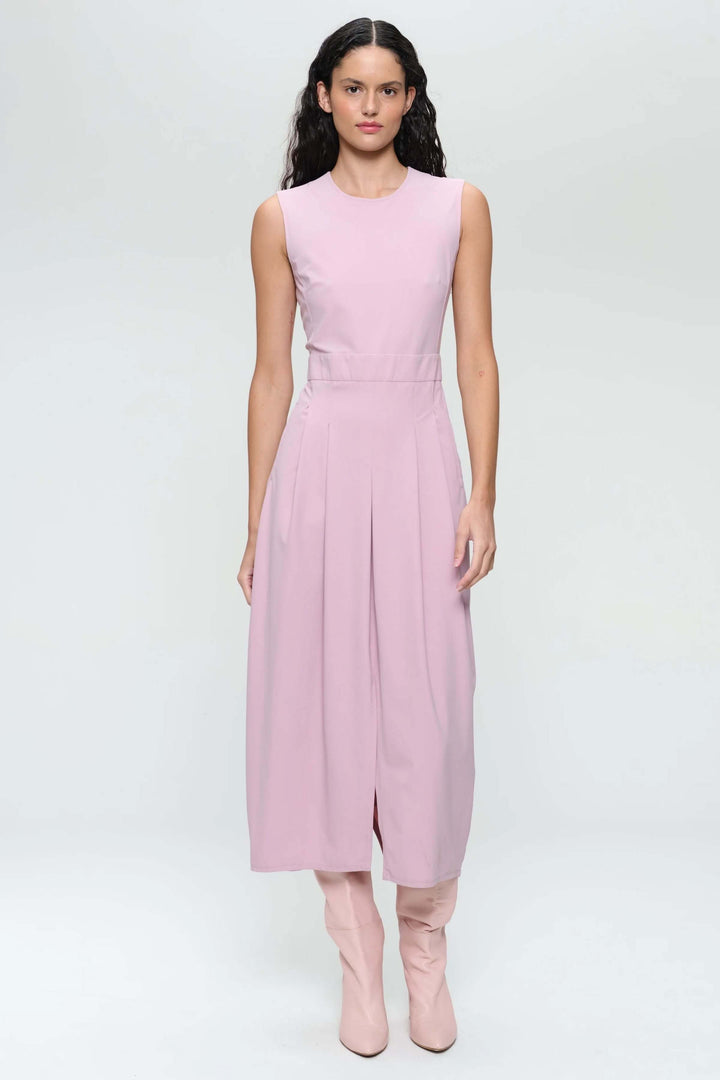 Robe longue sans manches rose avec encolure ronde et plis creux, portée avec des bottes hautes.