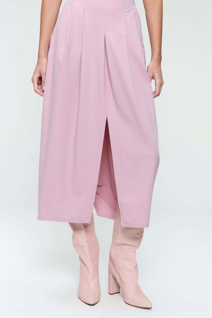 Robe longue façon midi rose avec plis creux, portée avec des bottes hautes pour un look moderne et élégant.