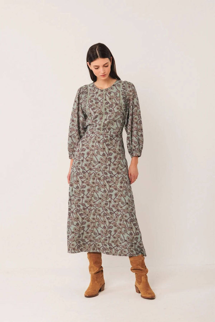 Femme portant une robe longue à motif géométrique avec manches bouffantes, encolure ronde, associée à des bottes en daim pour style bohème chic.
