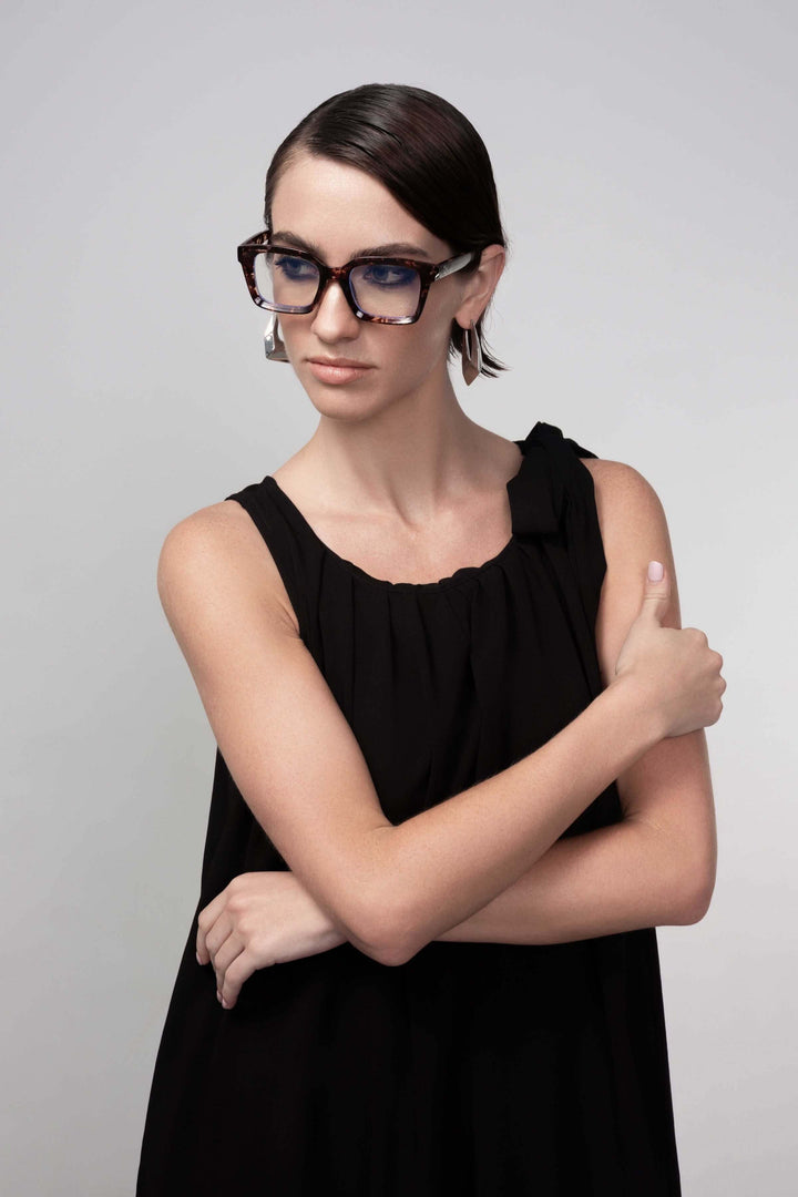 Femme portant une robe longue élégante noire sans manches avec lunettes de vue modernes, pose élégante sur fond neutre.