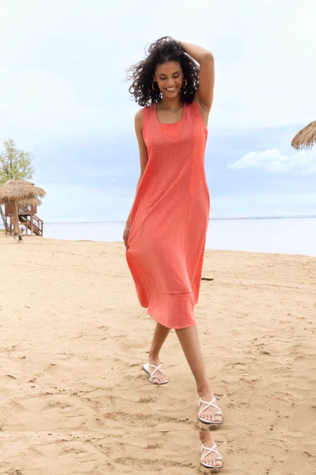 Femme en robe midi fluide à manches courtes marchant sur la plage, robe orange, encolure ouverte, style élégant et confortable.