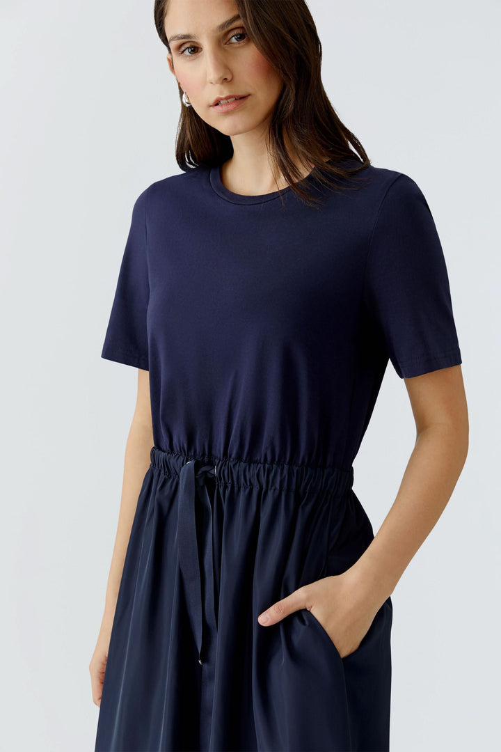Femme portant une robe midi à taille ajustable, style minimaliste avec manche courte et jupe fluide, idéale pour un look élégant.