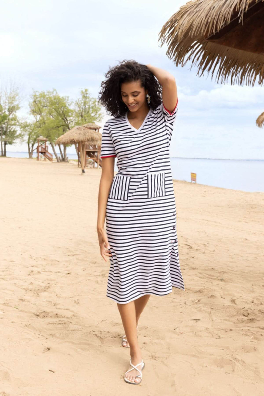 Femme portant une robe rayée à encolure en V sur une plage, style décontracté idéal pour l'été.
