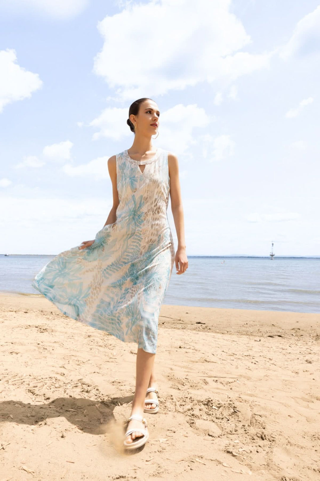 Femme portant une robe sans manches évasée avec imprimé nature sur une plage ensoleillée