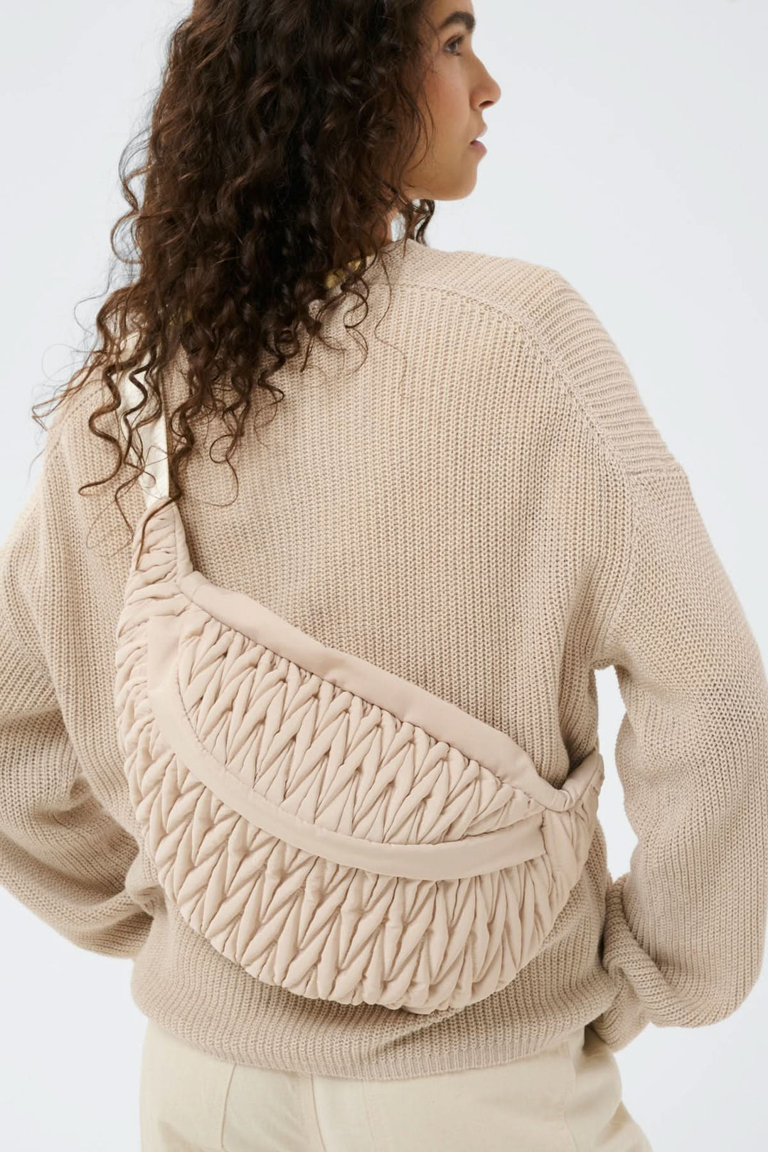 Femme portant le Sac bandoulière matelassé Samy Bumbag, texture froncée, beige, avec bandoulière ajustable, design moderne.