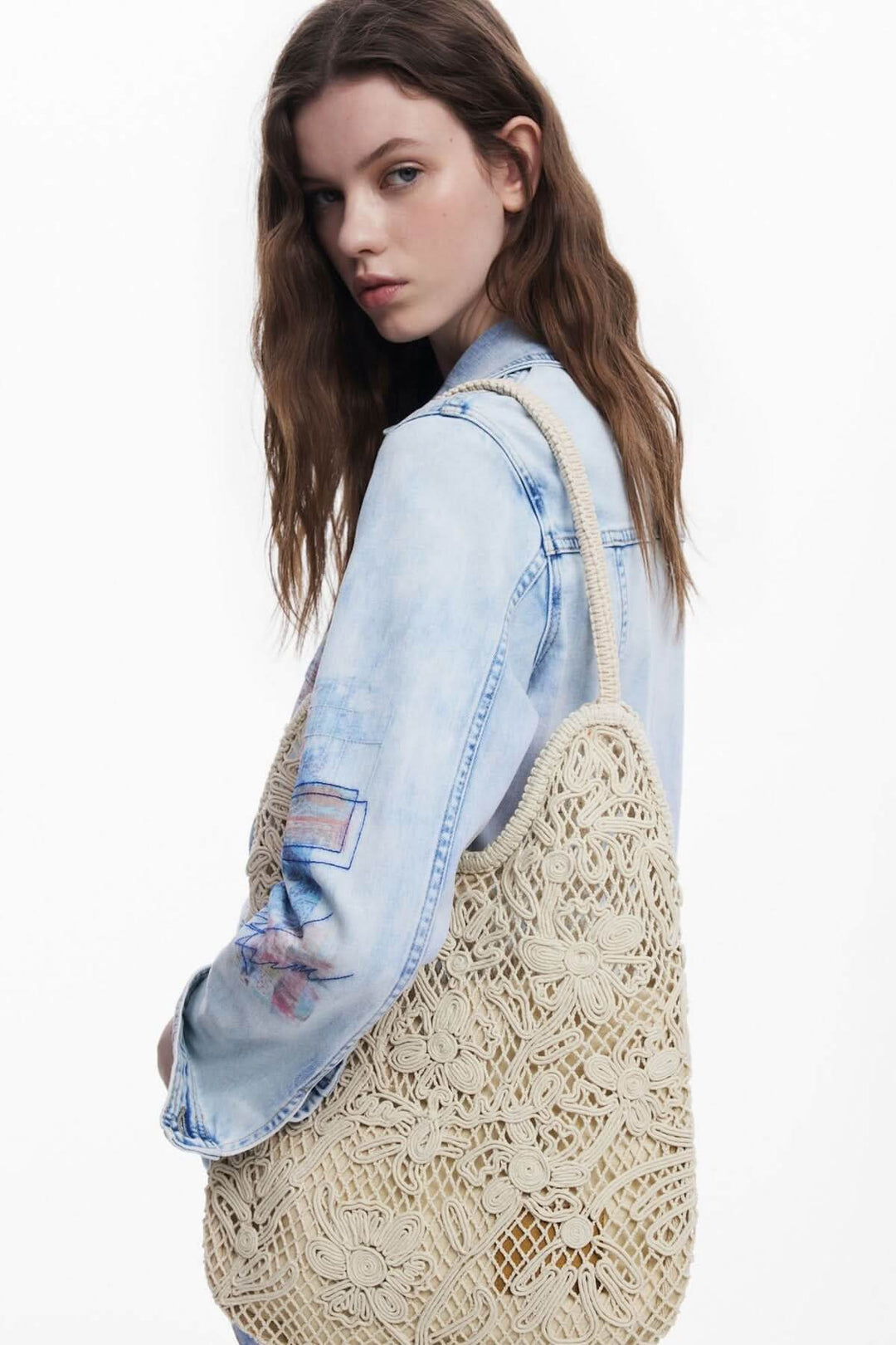 Sac en crochet ajouré aux motifs floraux, porté sur l'épaule d'un modèle, look bohème et élégant.