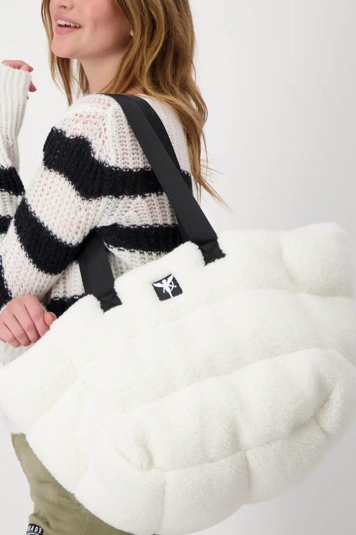 Sac en fourrure teddy blanc portant par une femme avec un pull rayé noir et blanc.