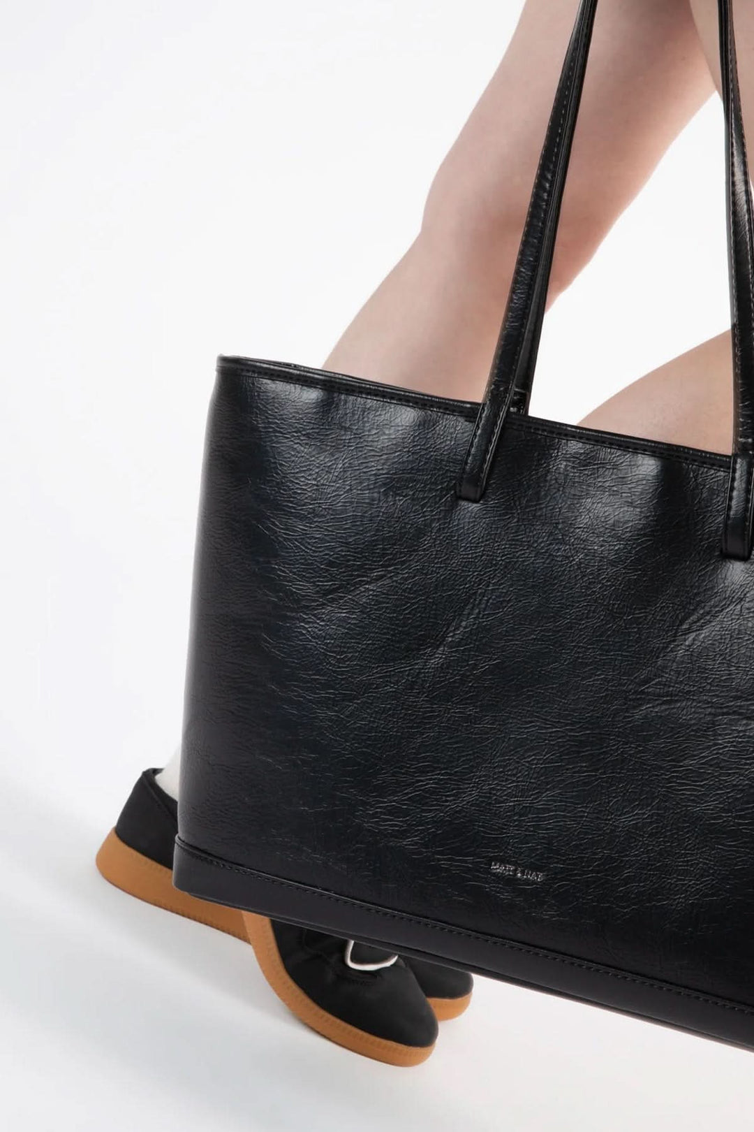 Sac fourre-tout Eliza noir avec anses, porté avec des chaussures modernes sur fond blanc.