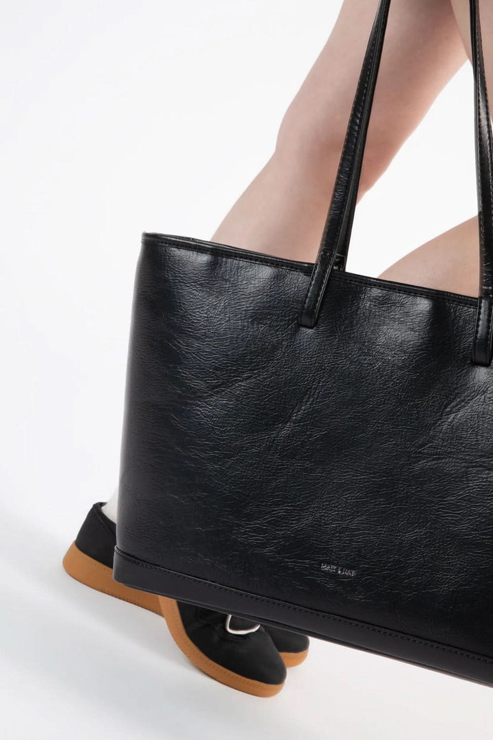 Sac fourre-tout Eliza noir avec anses, porté avec des chaussures modernes sur fond blanc.