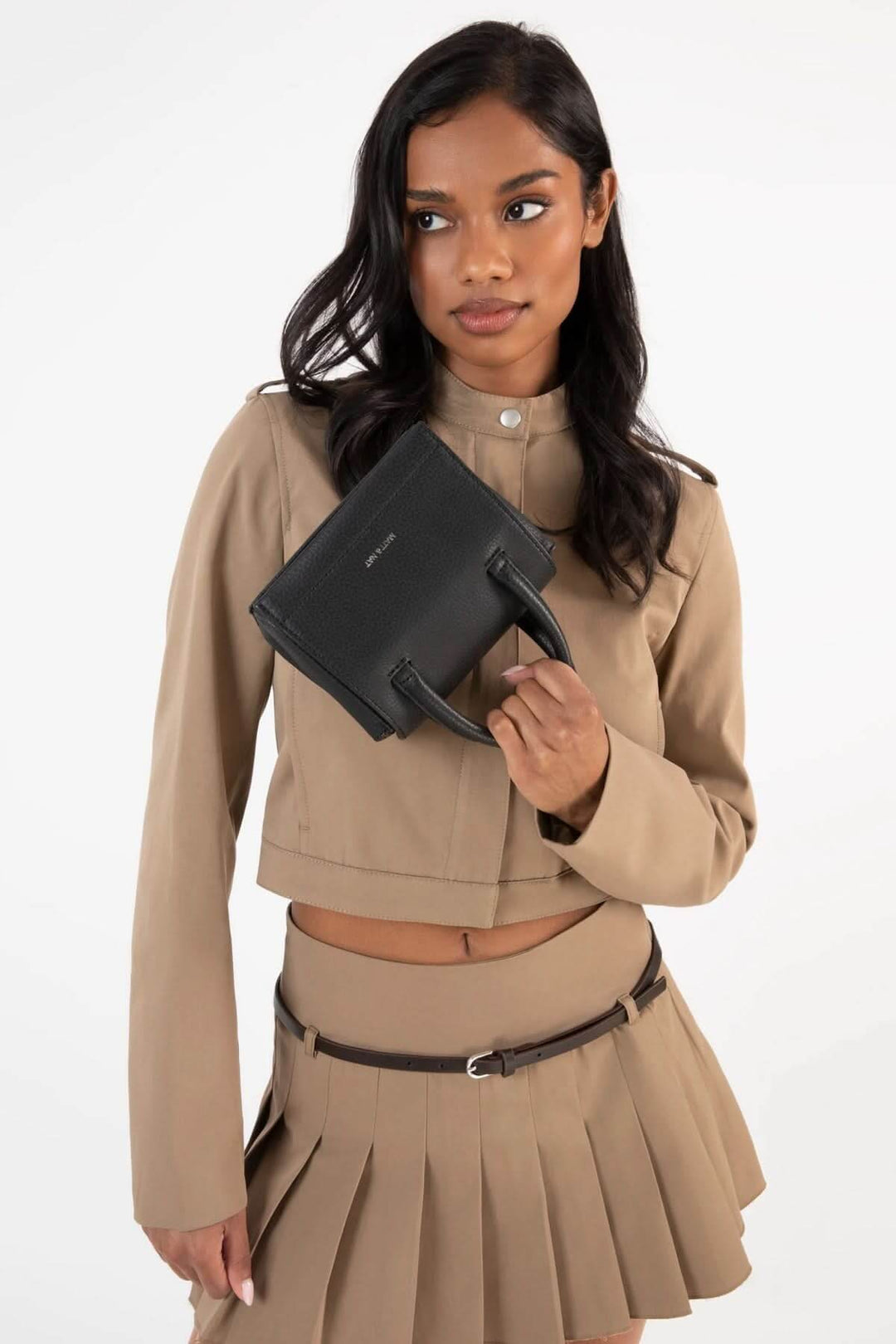 Femme portant une sacoche Adelmicro vegan noire avec des poignées, vêtu d'une tenue beige élégante.