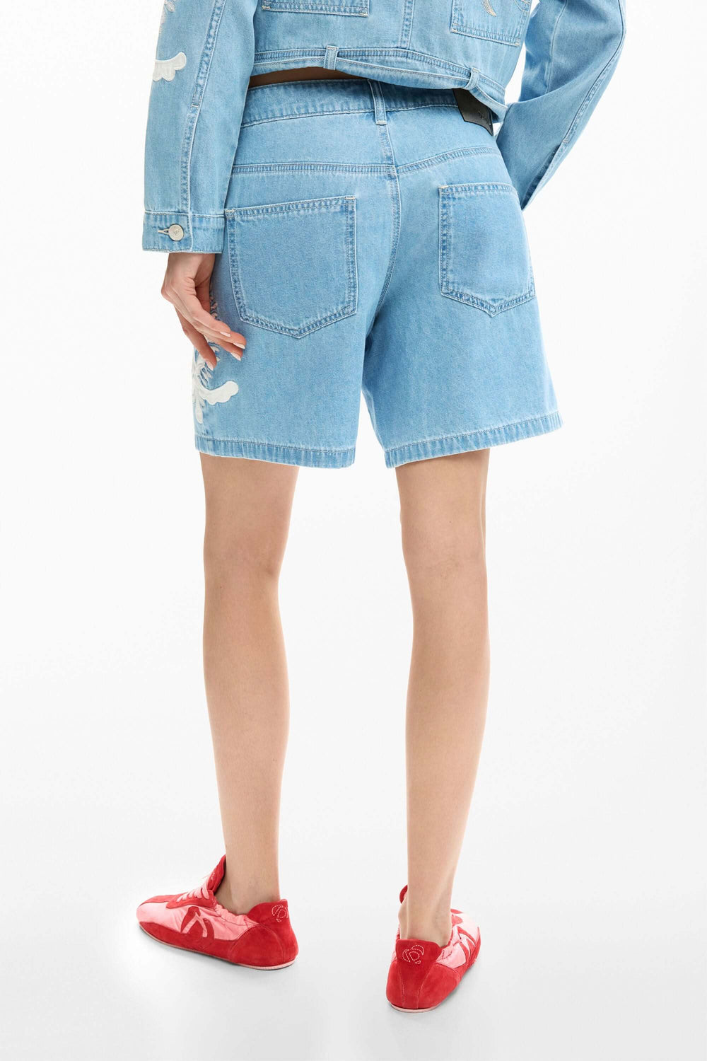 Short en jean brodée avec motifs, coupe droite, montré de dos avec poches, idéal pour un look estival confortable et stylé.
