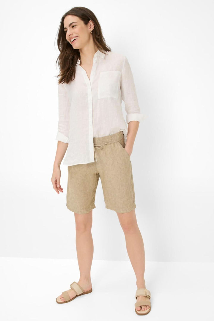 Femme en chemise blanche et short en lin beige, look décontracté et moderne pour un style sophistiqué.