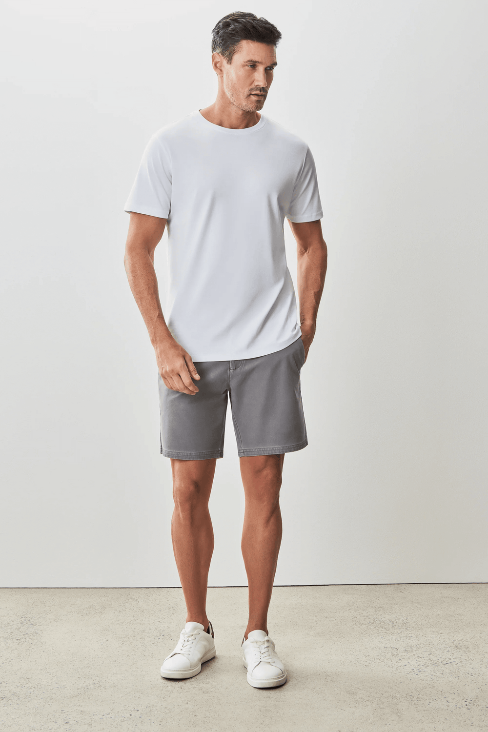Homme portant un t-shirt blanc moderne et élégant avec un short gris, style minimaliste.