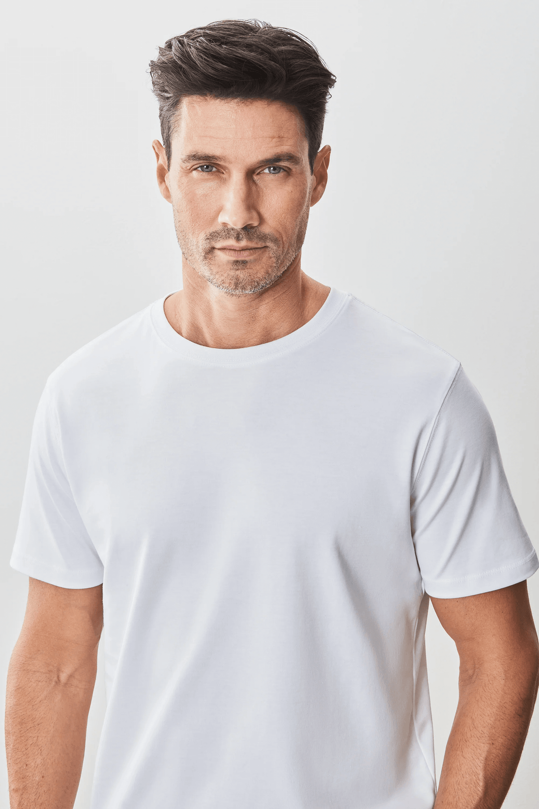 Homme portant un t-shirt blanc à manches courtes et encolure ronde, style minimaliste et moderne.