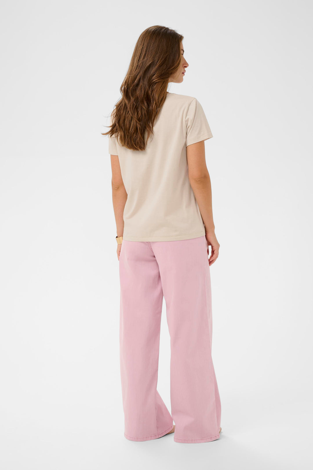 Femme portant un T-shirt Joliy beige avec manches courtes et coupe droite, assorti à un pantalon rose, vue de dos.