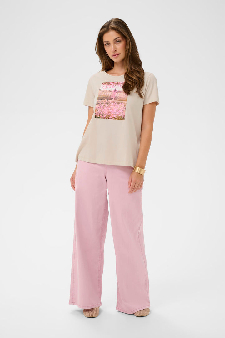 Femme portant un T-shirt Joliy à imprimé artistique, manches courtes et coupe droite, associé à un pantalon rose ample.