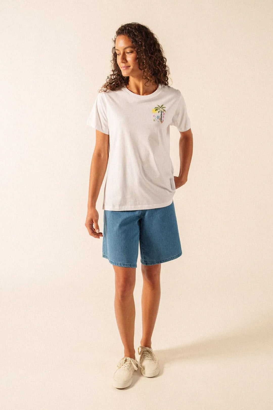 Femme portant le T-shirt Léonore blanc avec motif discret, assorti à un short en jean décontracté pour un look quotidien.