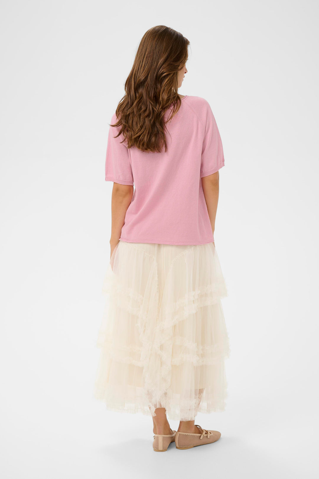 Femme portant le T-shirt Romane rose avec jupe longue, vue de dos, mettant en valeur la coupe décontractée et les manches amples du vêtement.