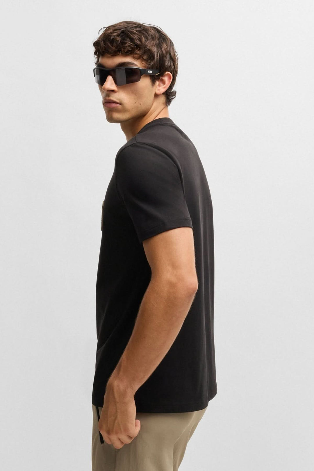 Homme portant un t-shirt noir avec logo, vue de dos, casual et stylé avec lunettes de soleil.