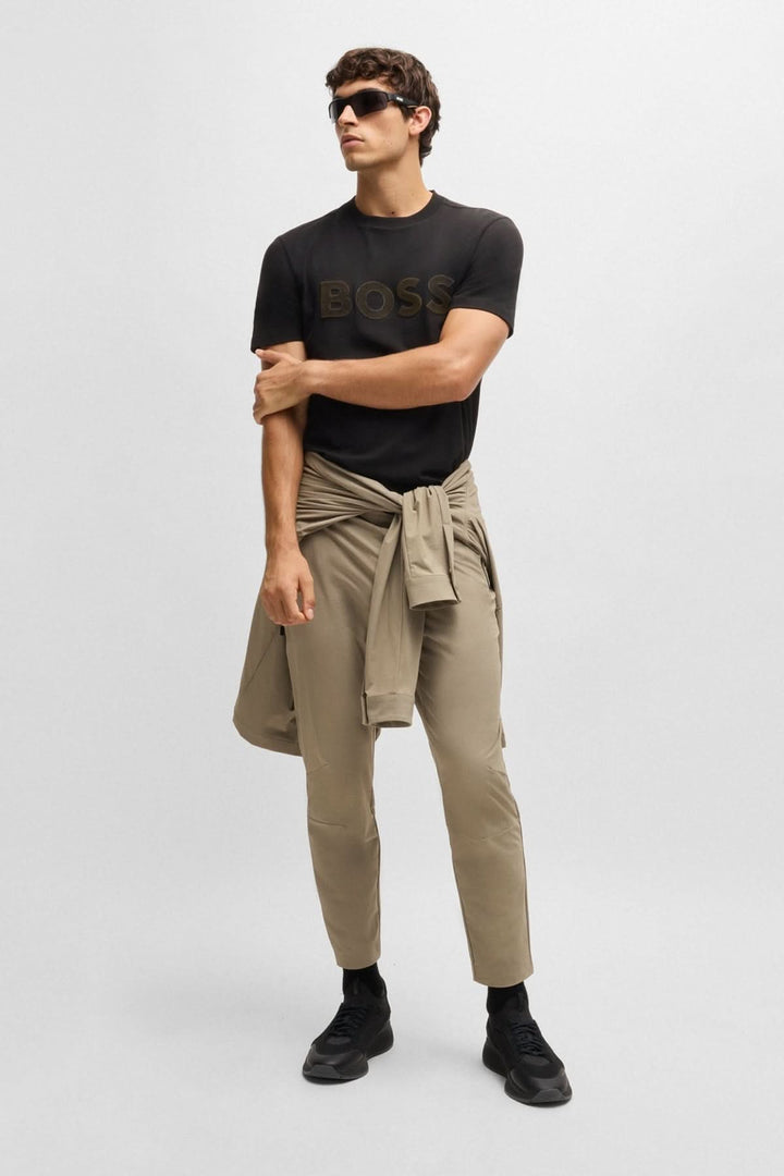 Homme portant un t-shirt noir avec logo BOSS en relief, pantalon beige et lunettes de soleil, look casual moderne.
