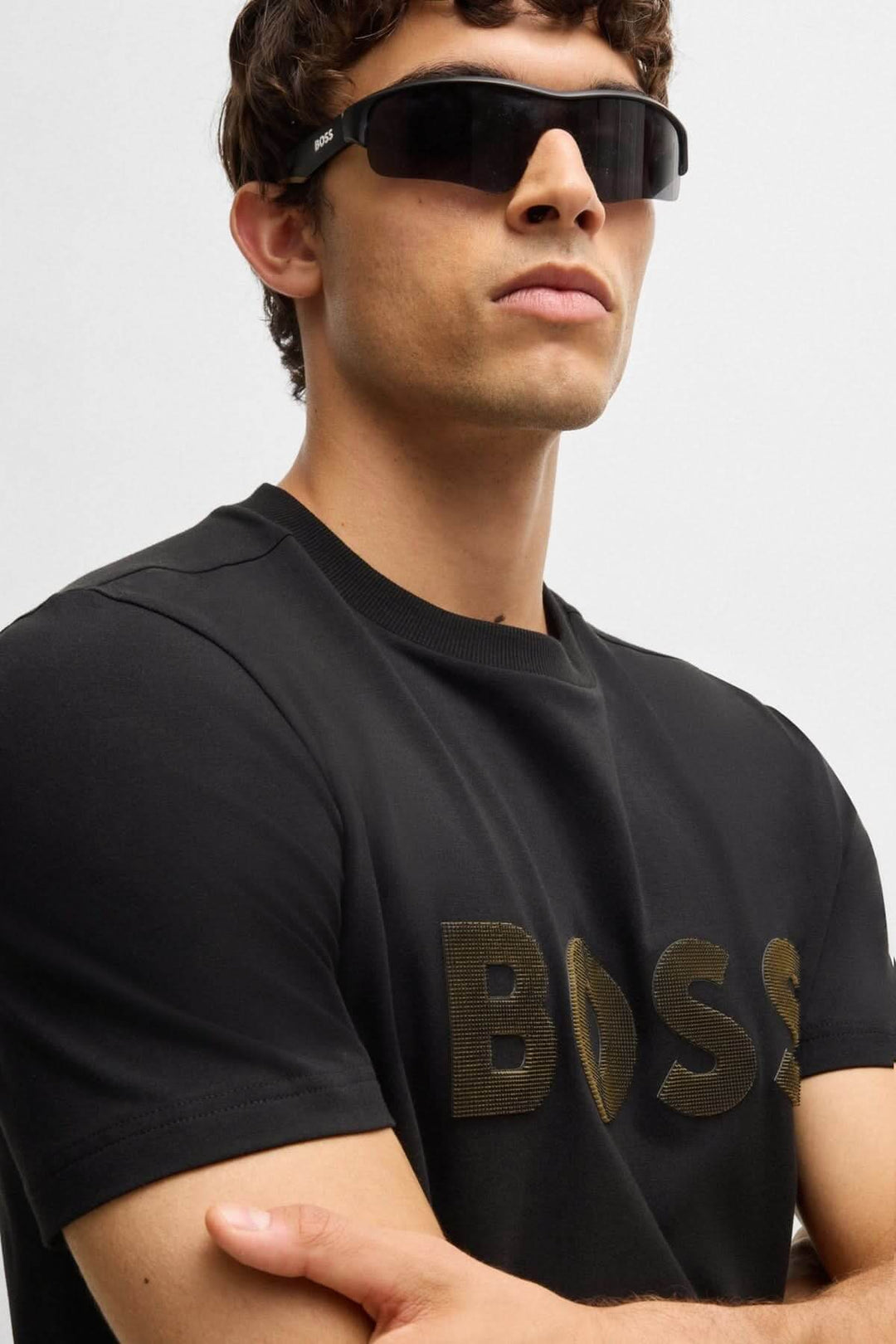 Homme portant un t-shirt noir avec logo BOSS en relief et lunettes de soleil.