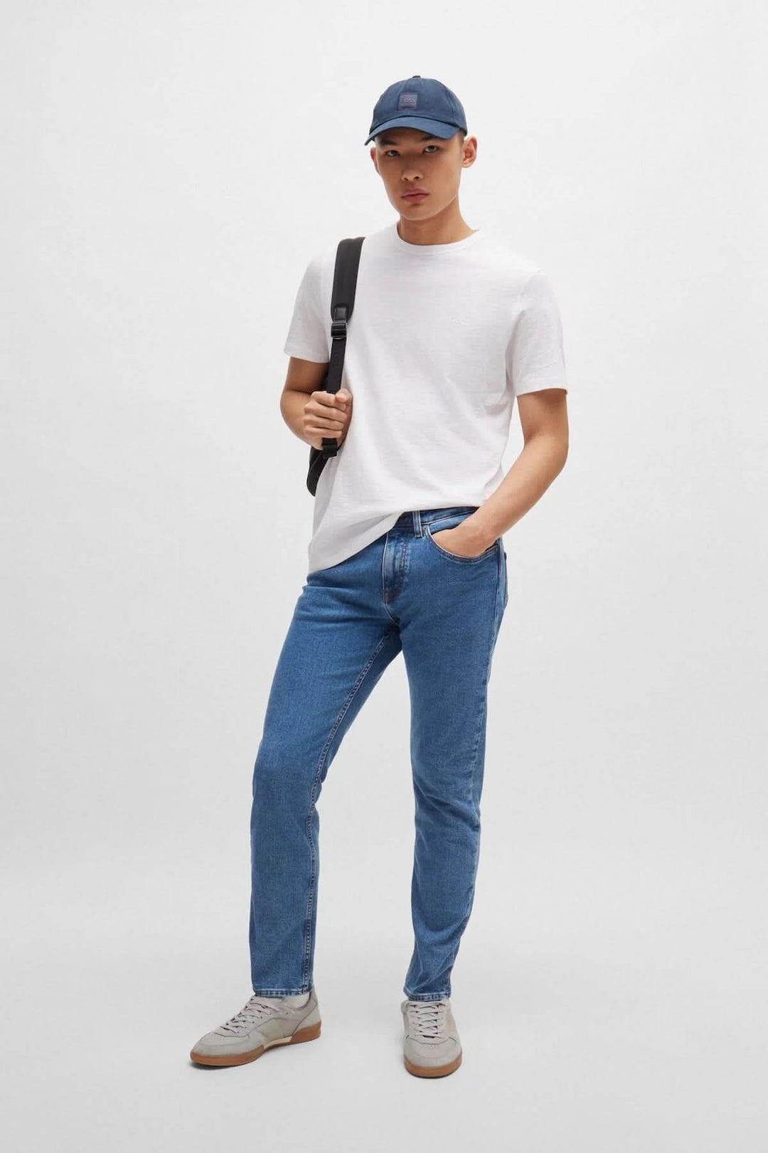 Homme portant un t-shirt blanc, jean bleu, et casquette, avec un sac à dos à l&