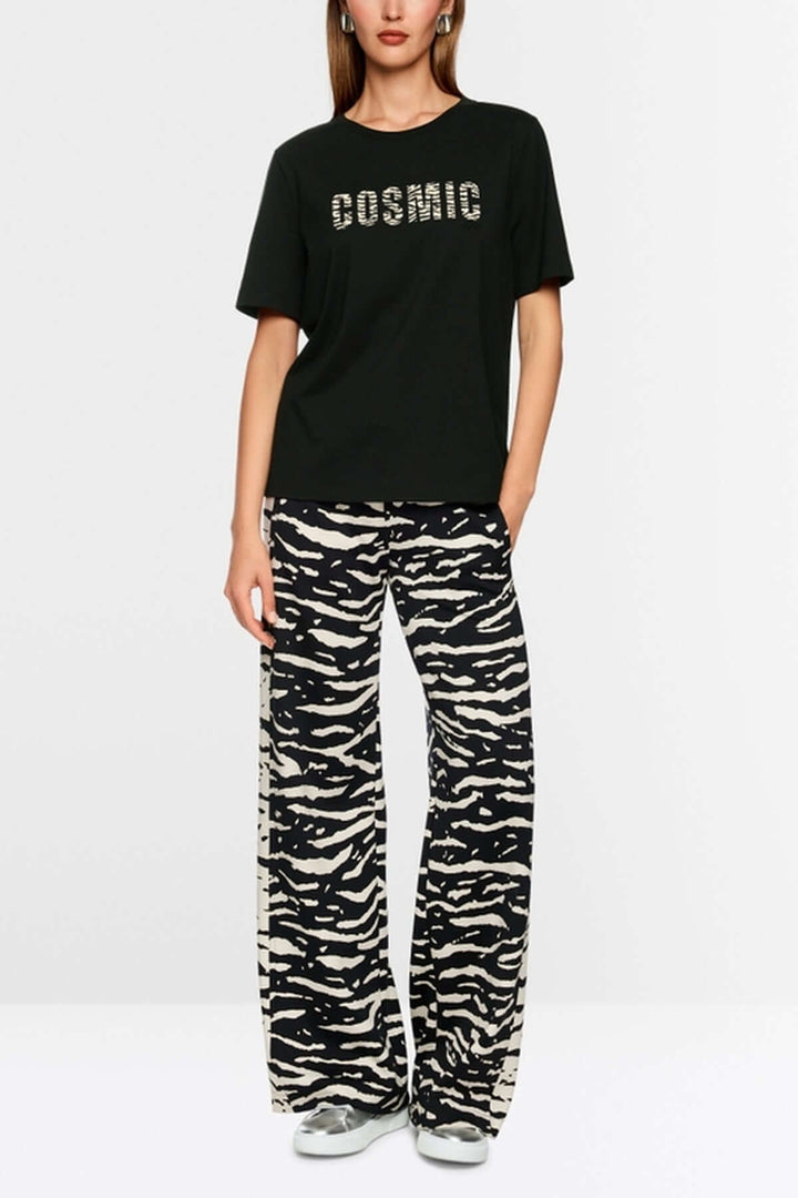 Femme portant un T-shirt classique col rond noir avec slogan « Cosmic Love » et pantalon imprimé animal. Fabriqué en coton biologique.