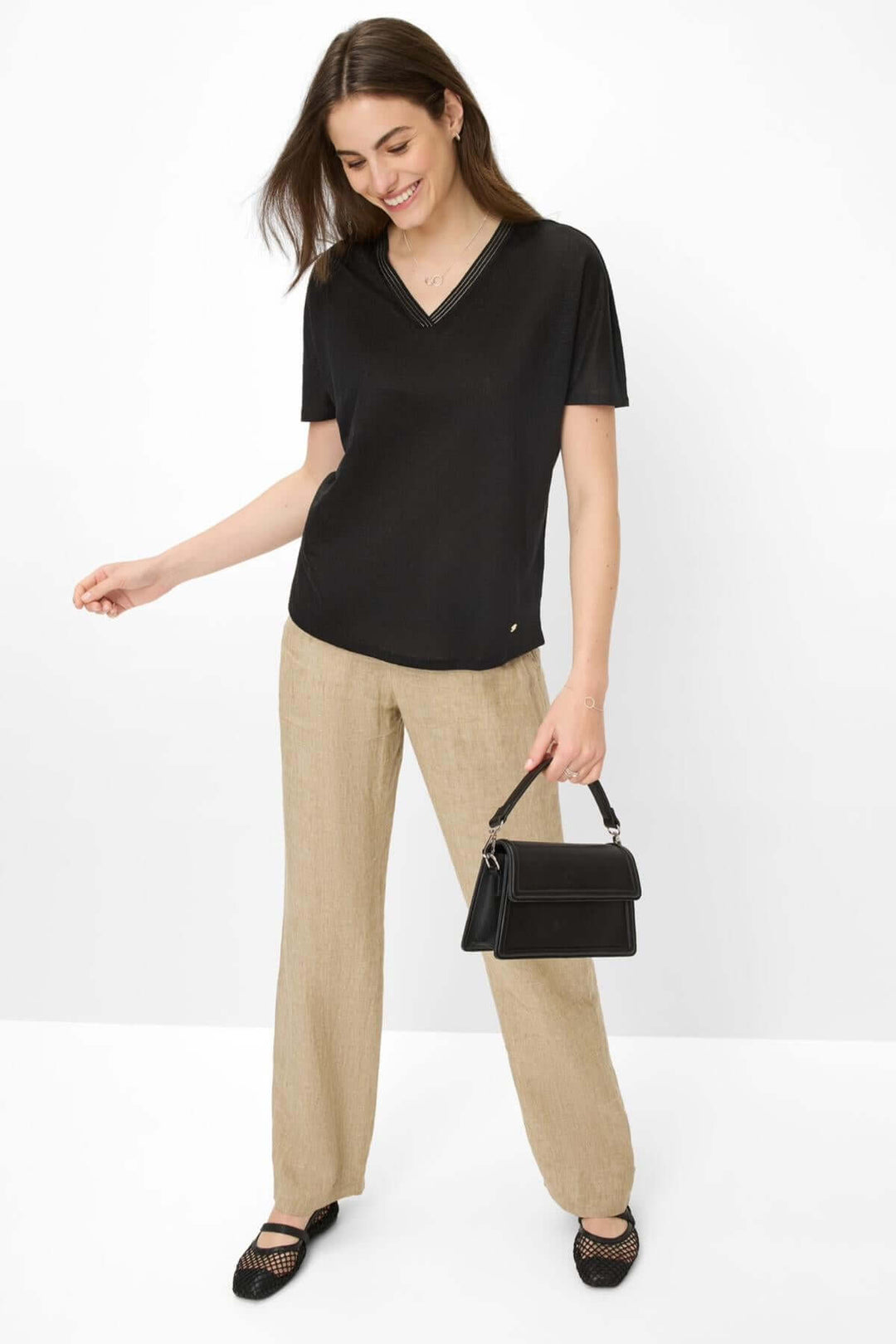 Femme portant un T-shirt col V noir et un pantalon beige, accessoirisé avec un sac à main élégant.