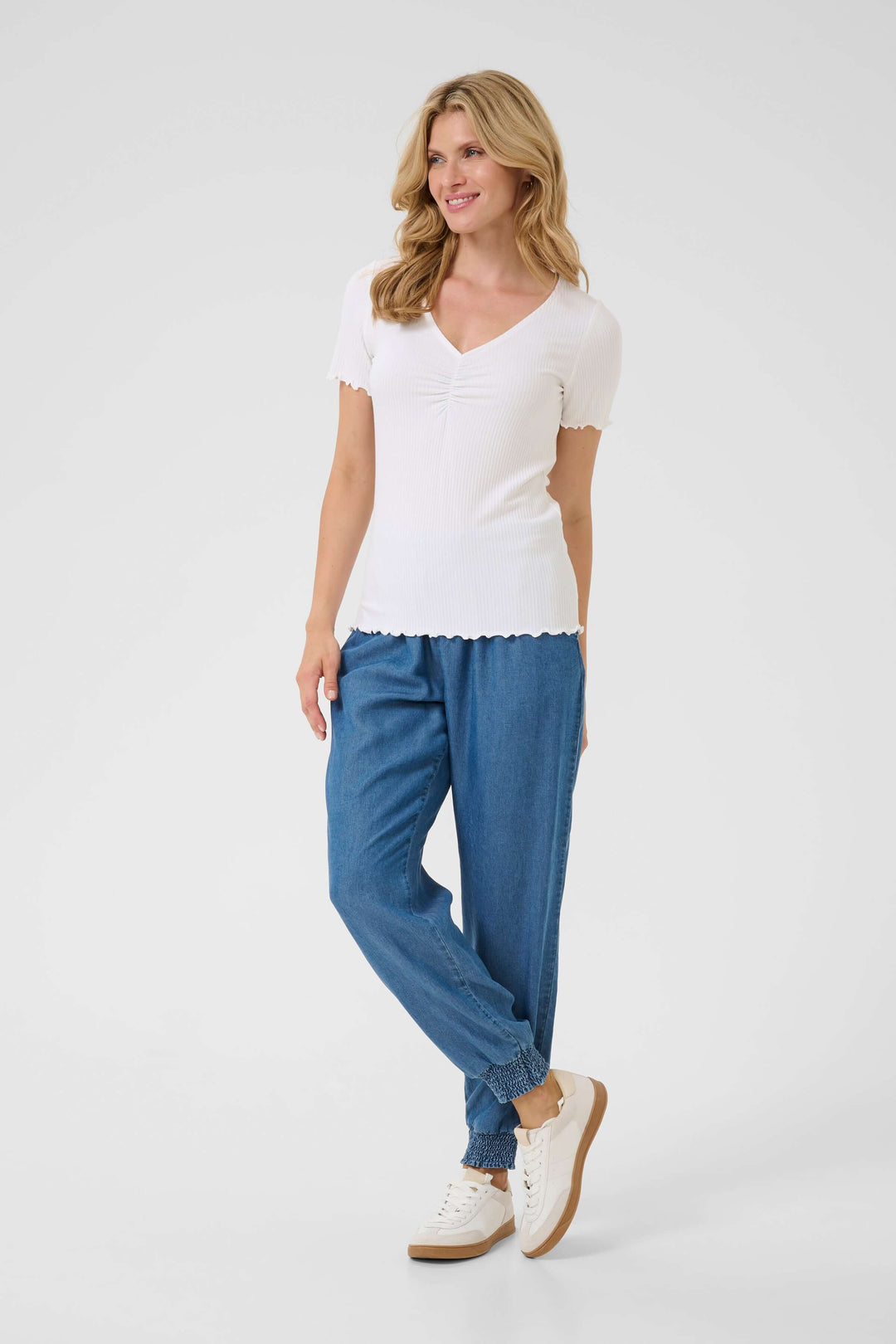 Femme portant un t-shirt blanc à col froncé et un pantalon en denim, style décontracté et élégant.